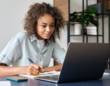 Teenager studying a virtual course on a laptop while writing notes